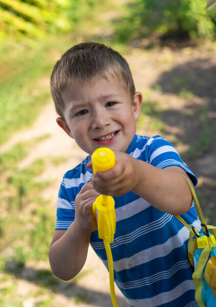 Игровой пятилетний мальчик с водяным пистолетом делает смешные лица и брызги воды в летнем парке на открытом воздухе, радостные детские моменты, активные развлечения на открытом воздухе и счастливый образ жизни детей. Высокое качество фото
