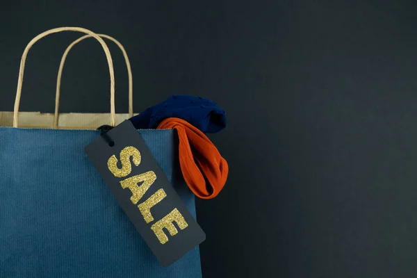 Blue paper bag with SALE label on black background. Sale concept. Copy space. New Year sales.