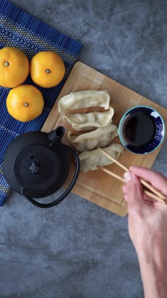 人的手用筷子蘸着中国菜酱汁 用茶壶和橙子装饰在石头的背景上 顶部视图 垂直录像 — 图库视频影像