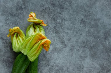 Three zucchini flowers piled on a stone background. Horizontal photo.