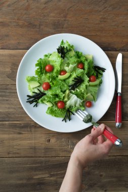 Tahta arka planda beyaz tabakta çatal yiyen bir salata. Uzayı kopyala Dikey fotoğraf. Üst görünüm.
