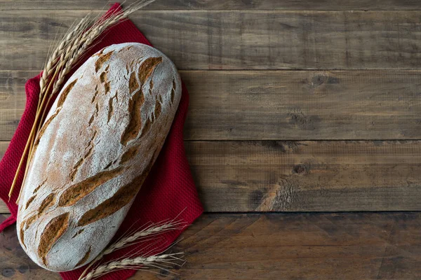 stock image Piece of rustic bread on wooden background with napkin decorations and ears of wheat. Copy space. Top view.