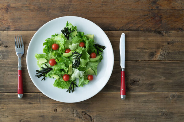Тарелка с разнообразным овощным салатом на белой тарелке на деревянном фоне. Принято. Вид сверху.