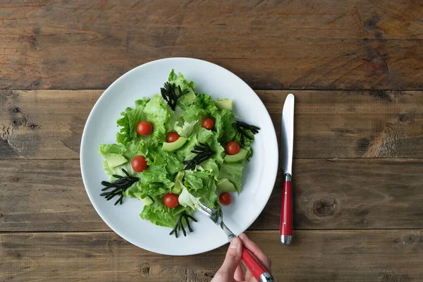 Tahta arka planda beyaz tabakta çatal yiyen bir salata. Uzayı kopyala Üst görünüm.
