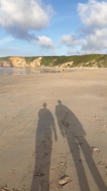 Sahilde yürüyen iki kişinin dikey gölge videosu. Hareket halindeki video.