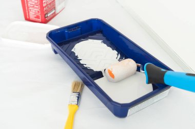 Mavi tepside boya silindirli beyaz bir duvar boyamak. Ev boyama işi. Boşluğu kopyala.