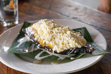 Üstünde muz ve yaprak ve peynir olan bir tabak yemek. Tabak ahşap bir masanın üzerinde.