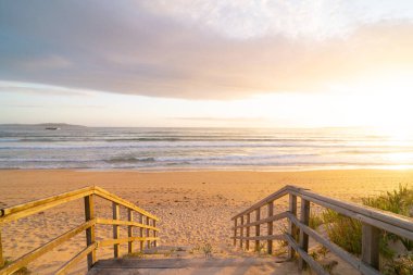 Suya giden tahta tahta kaldırımlı bir sahil. Gökyüzü bulutlu ve güneş batıyor.