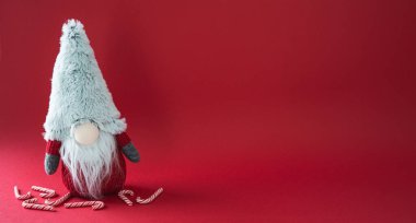 Mavi bir cüce kırmızı arka planda bir demet şeker kamışı ile oturuyor. Cüce kırmızı bir şapka ve gri bir sakal takıyor. Çubuk şekerler cücenin etrafına saçıldı ve bir şenlik yarattı.