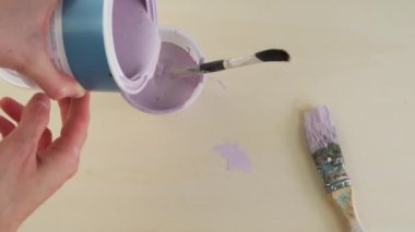 Bir boya fırçası boya kabına batırılır. Fırça masanın üstünde.