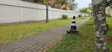 Beton yolun kenarındaki koni. Yol çevresindeki yeşil çimenler ve ağaçlar, arka plandaki duvarlar ve binalar.