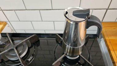 Siyah bir sobanın üstünde kahve makinesi. Arkaplanda beyaz kaplama