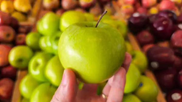 Diğer elmaların önünde yeşil bir elma tutmak. Lezzetli meyveler almak için pazar günü. Sağlığın için iyi olan lezzetli meyveler..