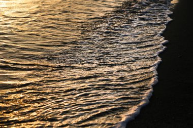 Gün batımında sahilde geometrik şekiller çizen dalgalar.