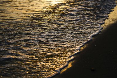 Gün batımında sahilde geometrik şekiller çizen dalgalar.