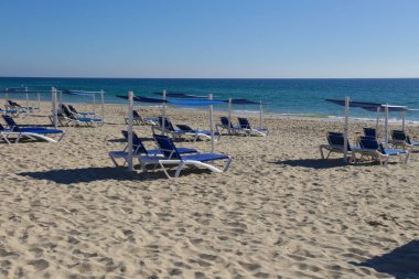 Portekiz 'deki Tavira Adası sahilinde şemsiyeli yalnız plaj sandalyeleri.