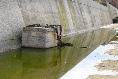 Portekiz 'in Sagres limanında yansıyan yeşil su birikintisinde paslı zincirli beton blok