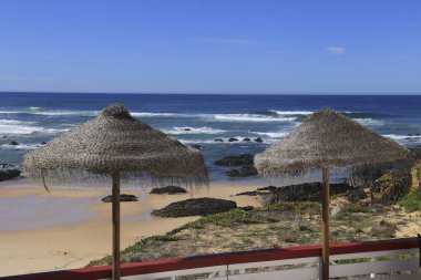 Almograve Sahili kıyısında saman şemsiyeli açık bar terası Vicentine Sahili, Alentejo, Portekiz