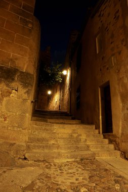 İspanya 'nın eski Caceres kasabasında gece vakti aydınlatılmış kaldırımlı sokaklar ve tarihi taş evlerin cepheleri