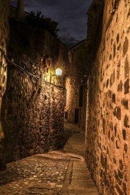 İspanya 'nın eski Caceres kasabasında gece vakti aydınlatılmış kaldırımlı sokaklar ve tarihi taş evlerin cepheleri