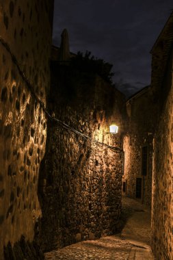 İspanya 'nın eski Caceres kasabasında gece vakti aydınlatılmış kaldırımlı sokaklar ve tarihi taş evlerin cepheleri