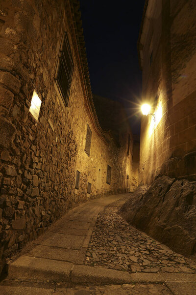 Illuminated cobbled streets and Facades of historic stone houses at night in the old town of Caceres , Spain