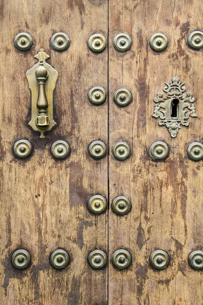 Forged metal vintage golden door knocker on brown wooden door in Cordoba, Spain