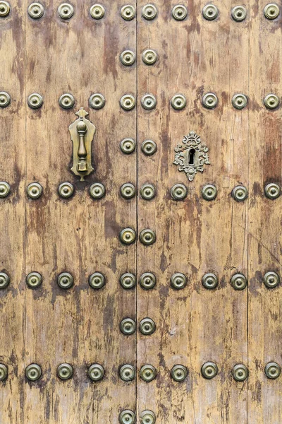 Forged metal vintage golden door knocker on brown wooden door in Cordoba, Spain