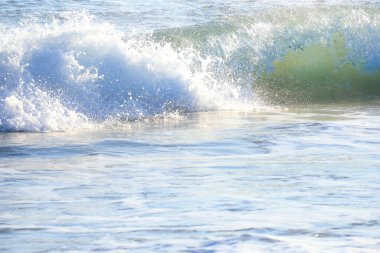 Güneşli bir günde sahilde dalgalar kopuyor.