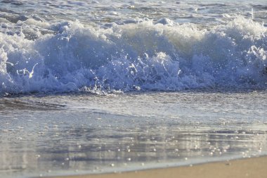 Güneşli bir günde sahilde dalgalar kopuyor.