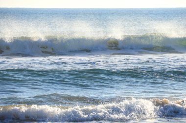 Güneşli bir günde sahilde dalgalar kopuyor.