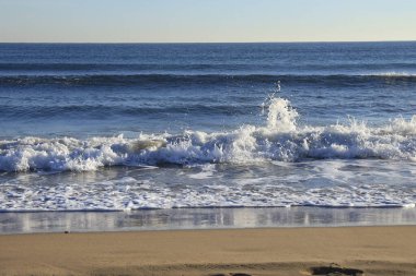 Güneşli bir günde sahilde dalgalar kopuyor.