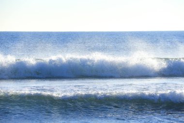 Güneşli bir günde sahilde dalgalar kopuyor.