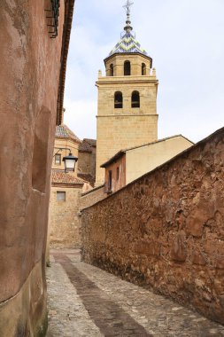 İspanya 'nın Teruel bölgesindeki Albarracin kasabasının arka planında eski cepheleri ve Salvador Katedrali olan dar bir sokak.