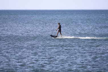 Denia, Alicante, İspanya - 18 Mayıs 2025: İspanya sahillerinde elektrikli ve motorlu sörf tahtası ile sörf yapan genç çocuk