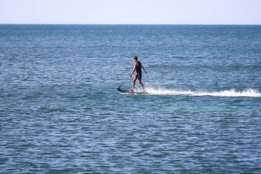 Denia, Alicante, İspanya - 18 Mayıs 2025: İspanya sahillerinde elektrikli ve motorlu sörf tahtası ile sörf yapan genç çocuk