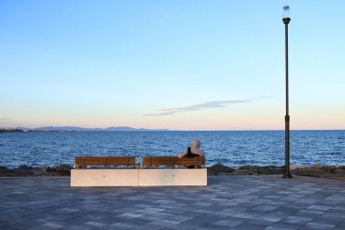 Kapüşonlu bir adam bankta oturuyor ve İspanya 'da denize bakıyor.