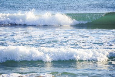 Güneşli bir günde sahilde dalgalar kopuyor.