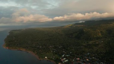 Tropikal adanın kıyı şeridi mavi gökyüzüne karşı yeşil ormanla kaplı bulutlar ve mavi deniz, hava manzaralı. Deniz Burnu: Okyanus ve gökyüzü. Filipinler, Camiguin.