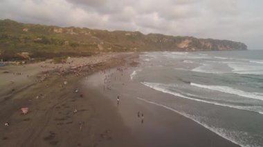 Okyanus kıyısında kumlu parangtritler, büyük dalgalar, gün batımında tropik tatil köylerinde yaşayan insanlar. Yogyakarta, Endonezya. Hava manzaralı deniz manzaralı, okyanus manzaralı ve güzel plajlı. Seyahat konsepti. Endonezya, java