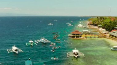 People snorkeling over coral reef in clear blue water from above. Moalboal, Philippines. People swim in the transparent sea between coral reefs. Summer and travel vacation concept.