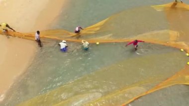Sri Lanka - August 25, 2021: Fishermen on the beach pulling net from sea to collect fishes. Trincomalee.