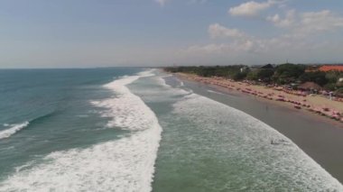 Dinlenen insanlar, oteller ve turistler, güneş şemsiyeleri, Bali, Kuta ile hava manzaralı kumsal. Su yüzeyindeki sörfçüler. Deniz manzarası, sahil, okyanus, gökyüzü deniz yolculuğu konsepti