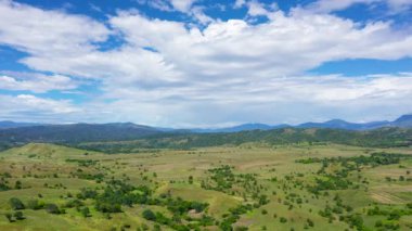 Aerial view of hills and mountains covered with green grass and rainforest against a background of blue sky and clouds. Philippines, Luzon. Summer landscape.