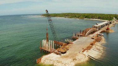 İnşaat alanındaki yük makinası. Körfez boyunca inşa halindeki köprü ve köprüde işçilerle birlikte inşaat ekipmanları. Siargao, Filipinler.