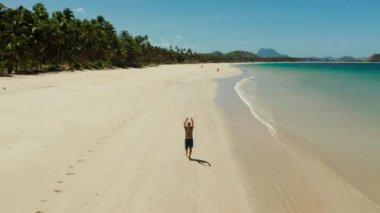 adam elini sallar ve onu takip etmek için arar. turist geniş bir tropikal kumlu plajda yürür ve eğlenceli. Nacpan, El Nido, Palawan, Filipinler