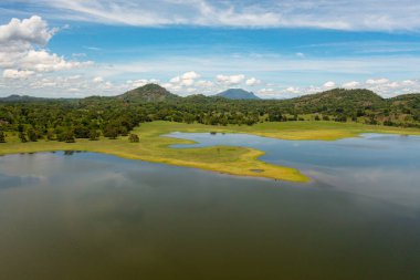 Top view of valley with a lake and tropical vegetation against a blue sky and clouds. Sorabora lake, Sri Lanka.