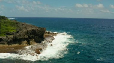 Adanın kıyı şeridi ve dalgalarla dalgalar kayalık bir sahile çarpıyor. Yavaş çekim, hava manzarası. Siargao, Filipinler. Yaz ve seyahat tatil konsepti