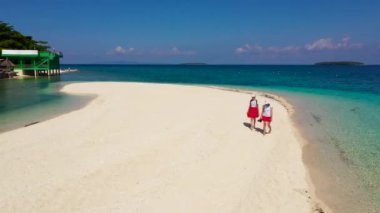 Kız turistler tropik bir plajda geziniyorlar. Mükemmel beyaz kumsal, yukarıdan manzara. Himokilan Adası, Leyte Adası, Filipinler. Turkuaz gölü olan beyaz kumlu plaj. Yaz tatili