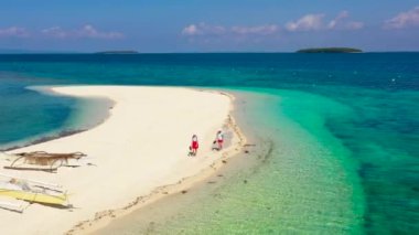 Kız turistler tropik bir plajda geziniyorlar. Mükemmel beyaz kumsal, yukarıdan manzara. Himokilan Adası, Leyte Adası, Filipinler. Turkuaz gölü olan beyaz kumlu plaj. Yaz tatili